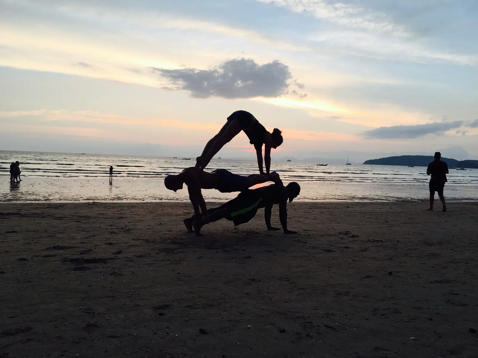Three people doing acro yoga in silhouette on Khanom Beach at sunset