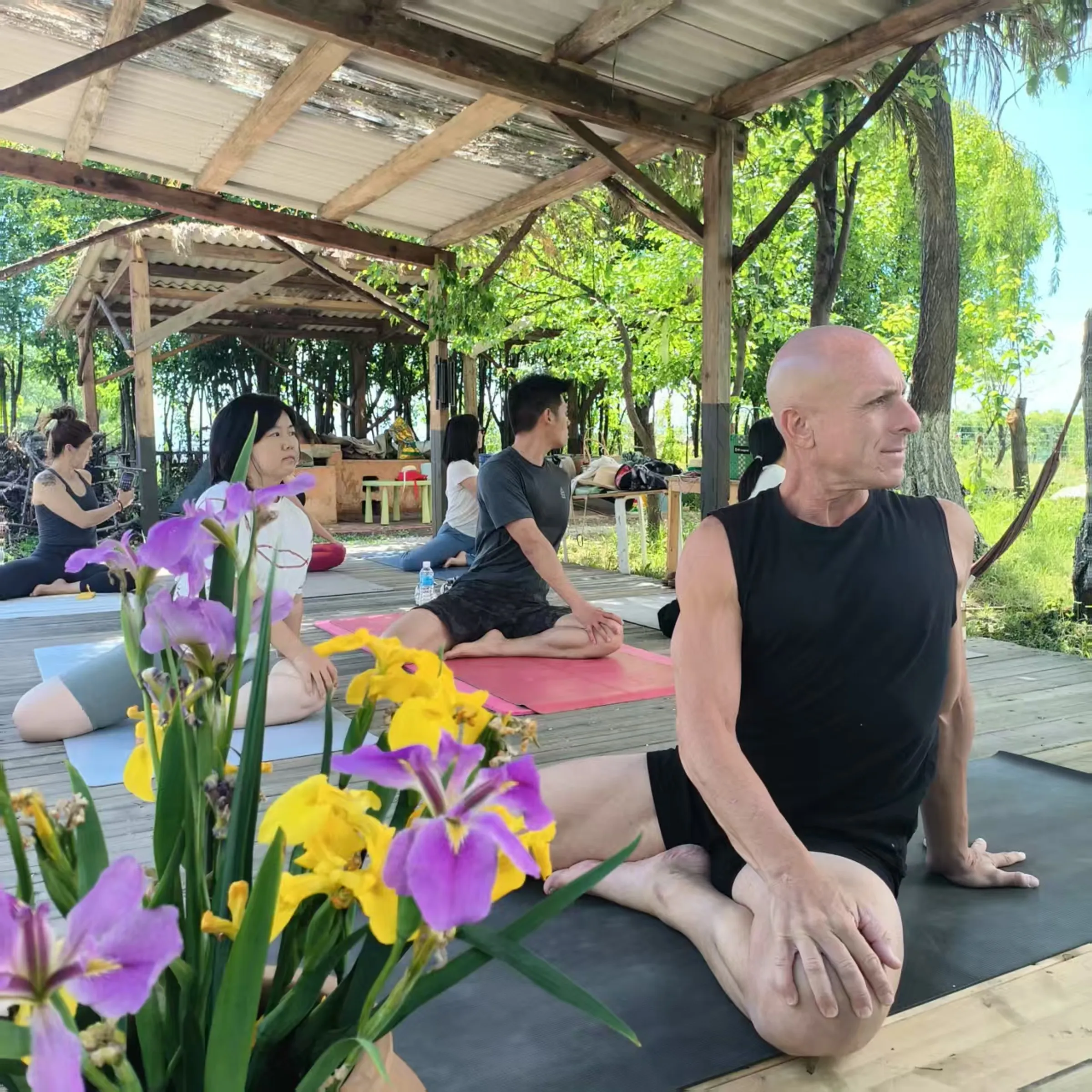 Gabe leading an outdoor spinal twist among flowers